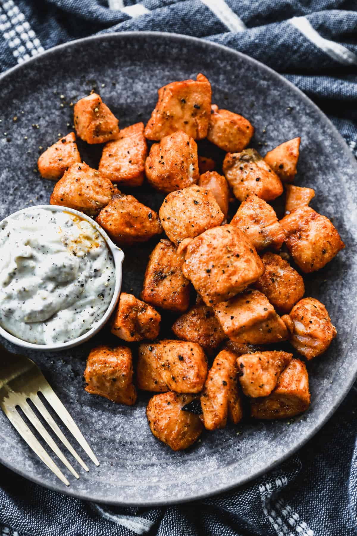 Air fryer salmon bites on a plate with a small bowl or remoulade sauce, for dipping.