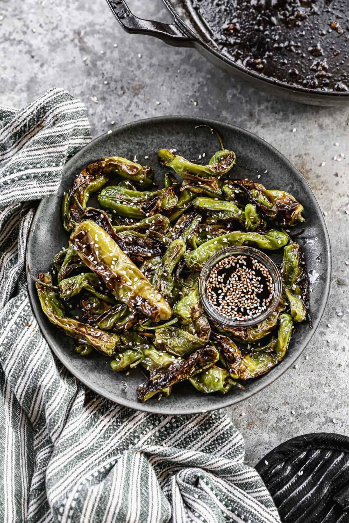 A plate full of easy Blistered Shishito Peppers, sprinkled with sesame seeds and served with a sesame dip.