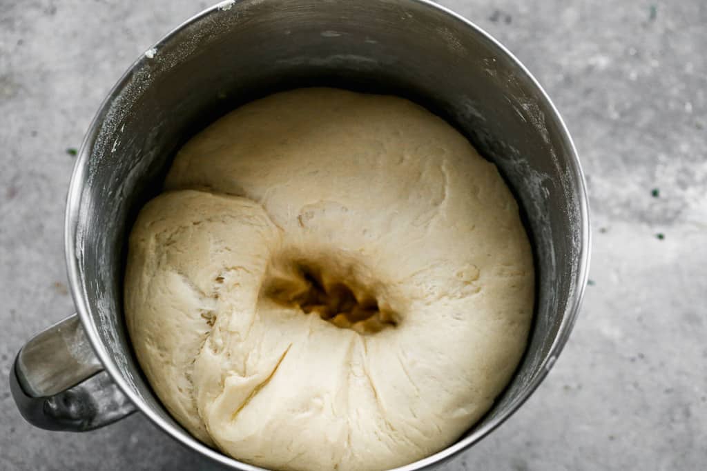 Risen bread dough in a bowl, punched down once, leaving an imprint.