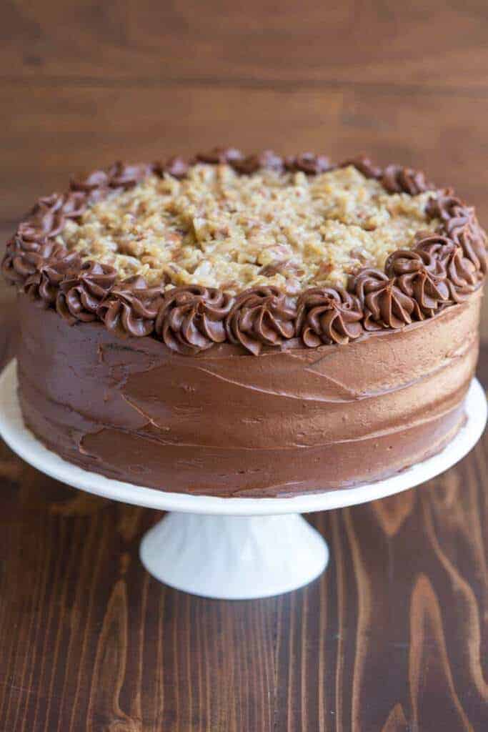 A full frosted and decorated German Chocolate served on a white cake stand.