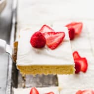 A square of the best White Sheet Cake being lifted from a pan, with a raspberry and sliced strawberries on top.
